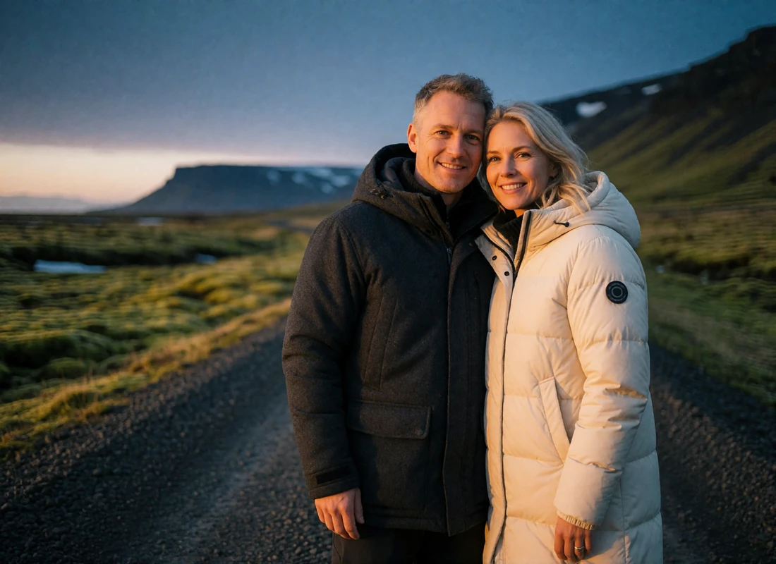 Couple standing close together on a gravel track in a wide Icelandic valley at dusk, mountains fading into twilight behind them